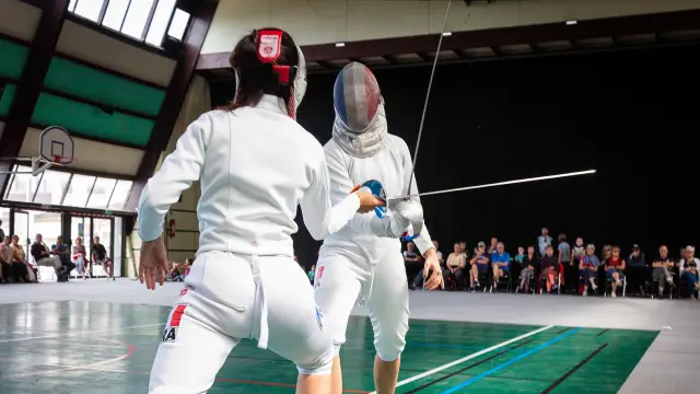 Deux sabreuses en tenue d'escrime s'affrontant lors d'un entraînement dans un gymnase.