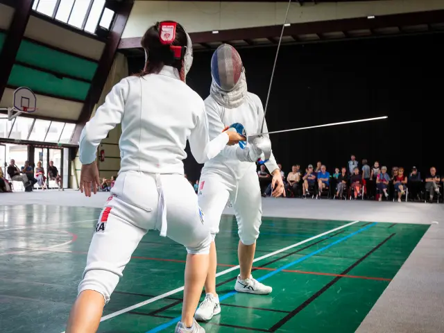 Deux sabreuses en tenue d'escrime s'affrontant lors d'un entraînement dans un gymnase.